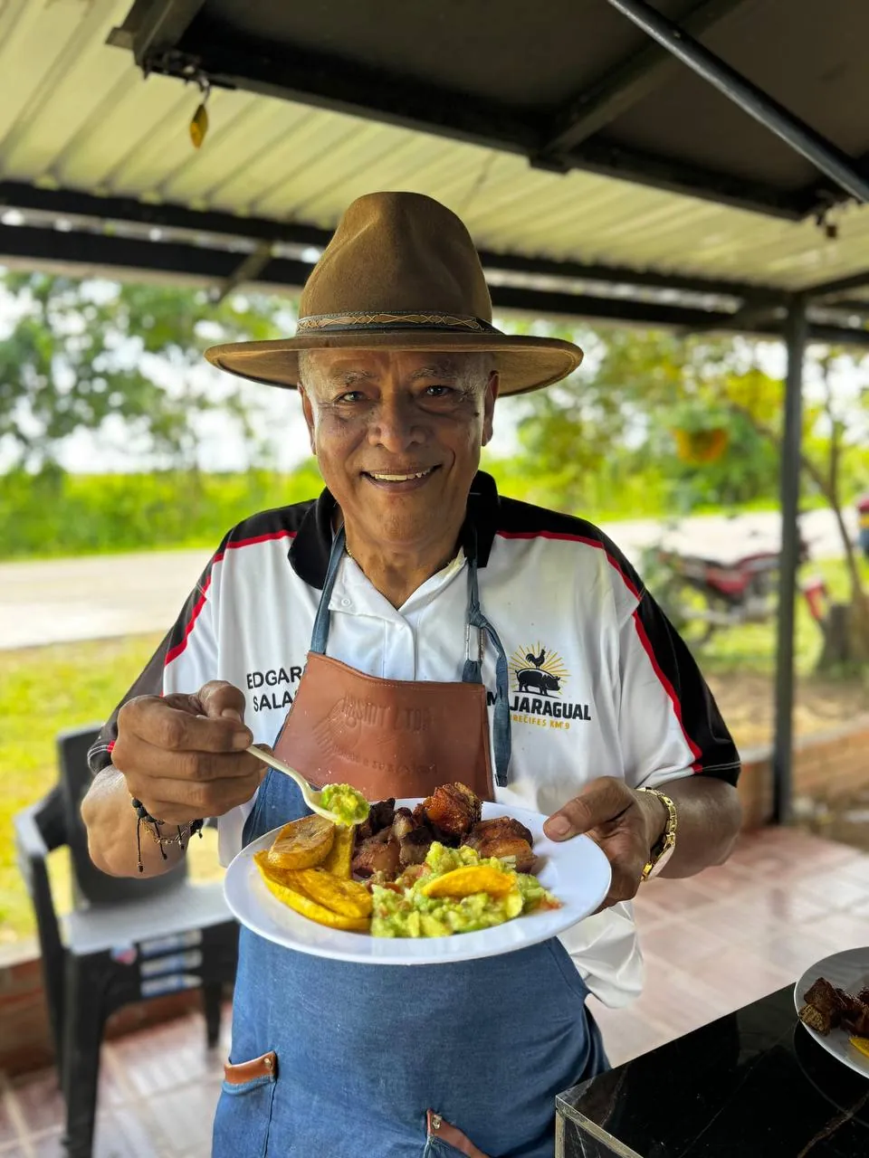 Don Edgar, dueño de Mi Jaragual, sirviendo un plato de asado con papa y ensalada